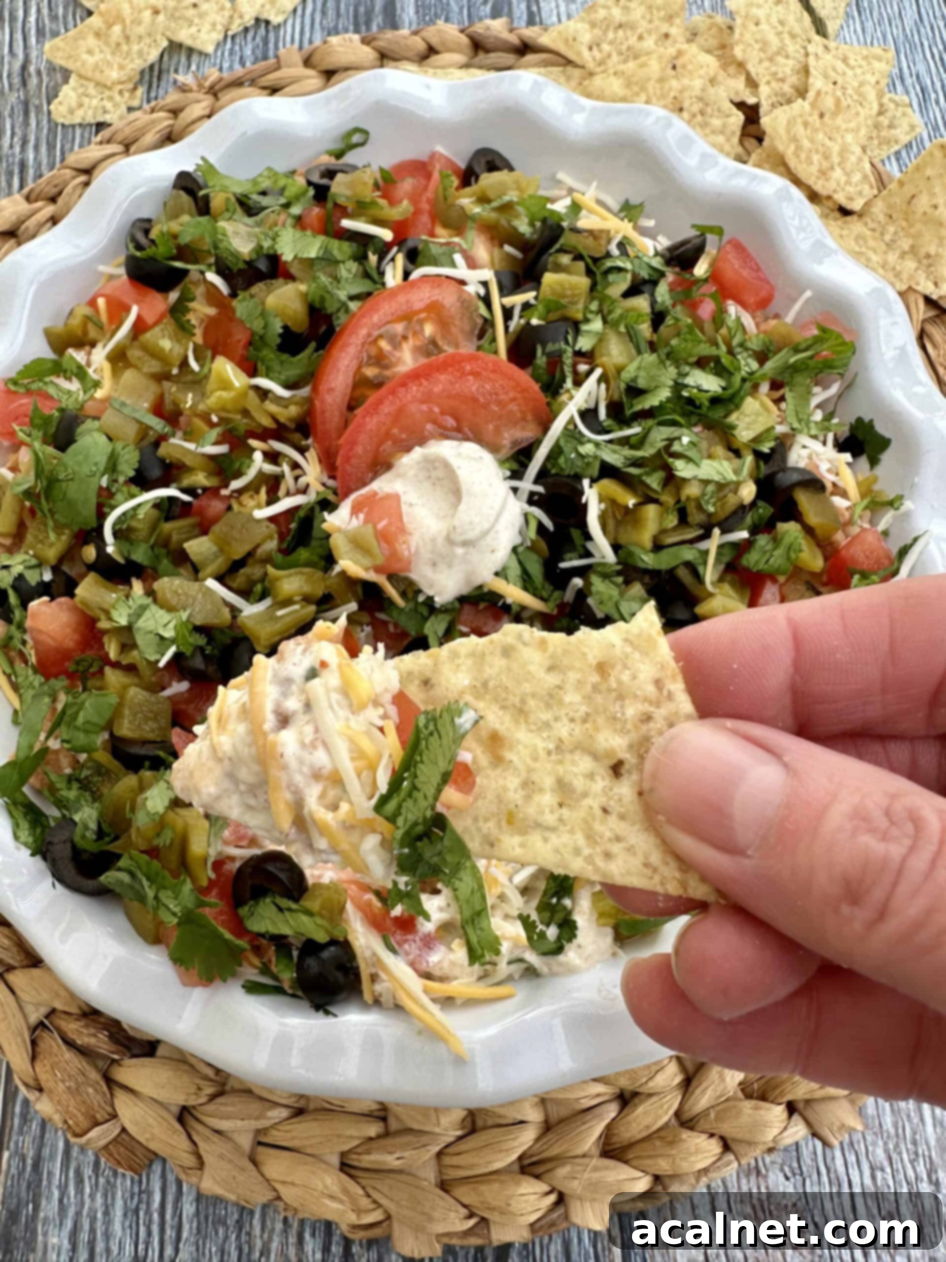 A hand holding a chip scooping up a generous serving of 5 layer taco dip, showing all the distinct layers.