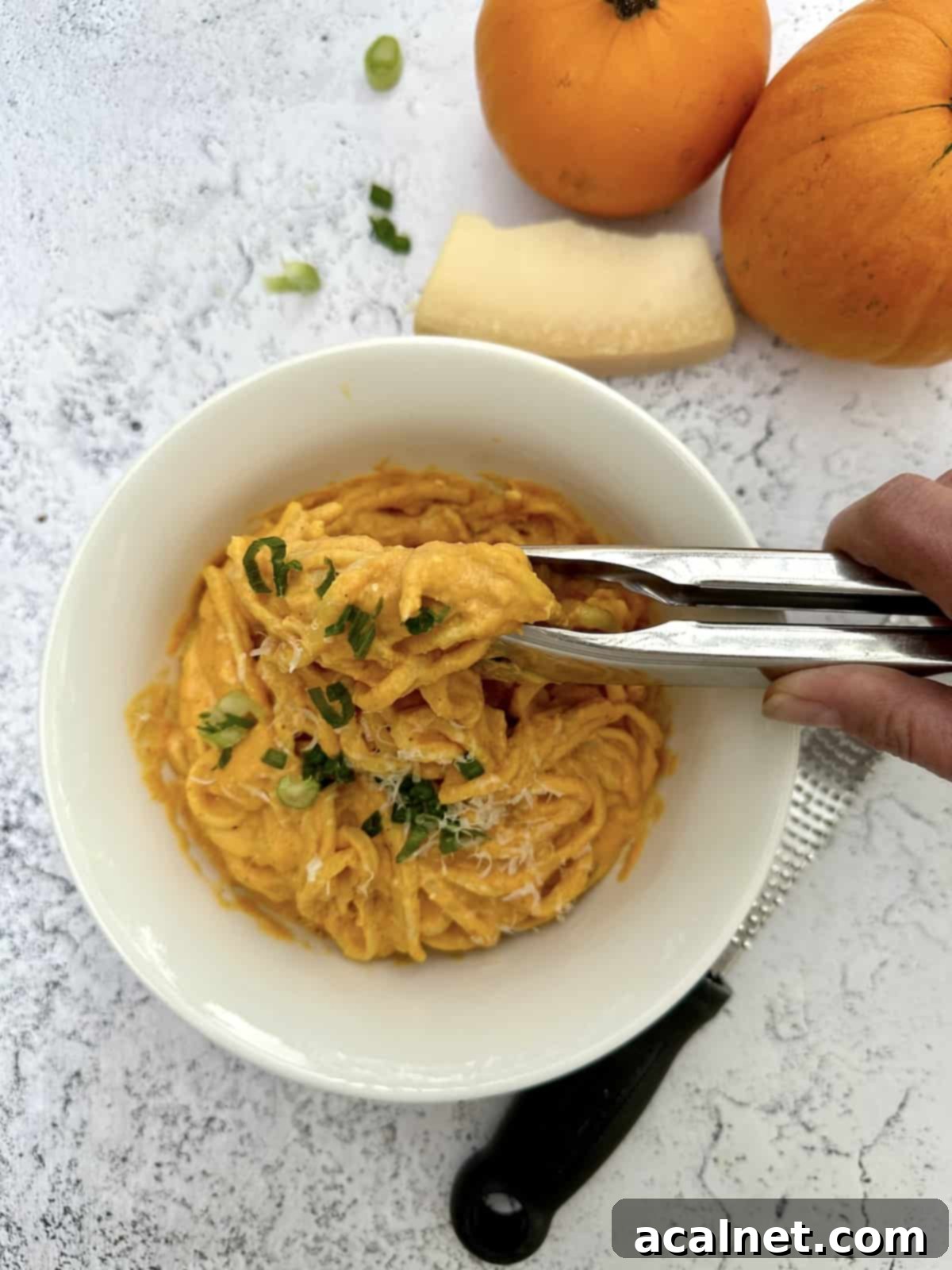 Pumpkin sauce with pasta in a bowl with pumkins and a wedge of parmesan cheese on the side.