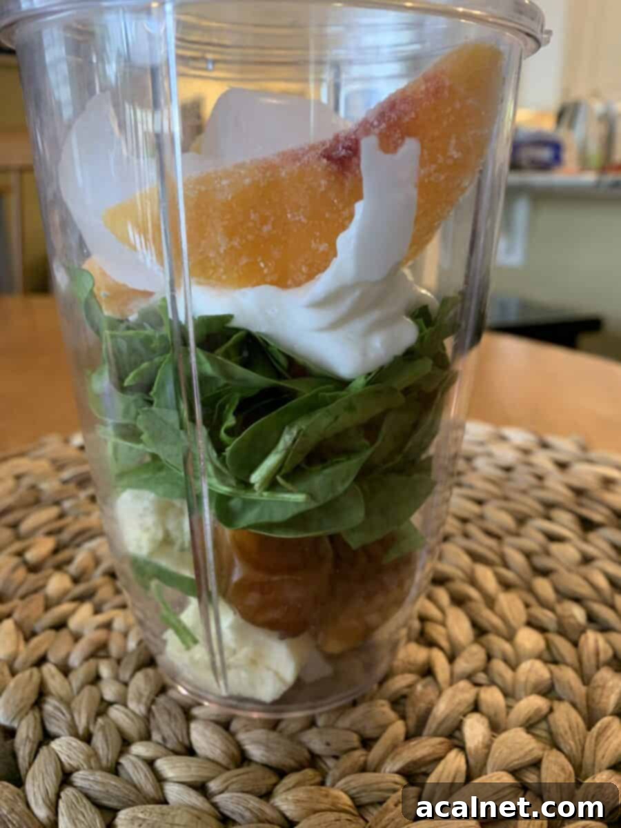 Peach slices on top of smoothie ingredients in a blender cup, ready to be blended.