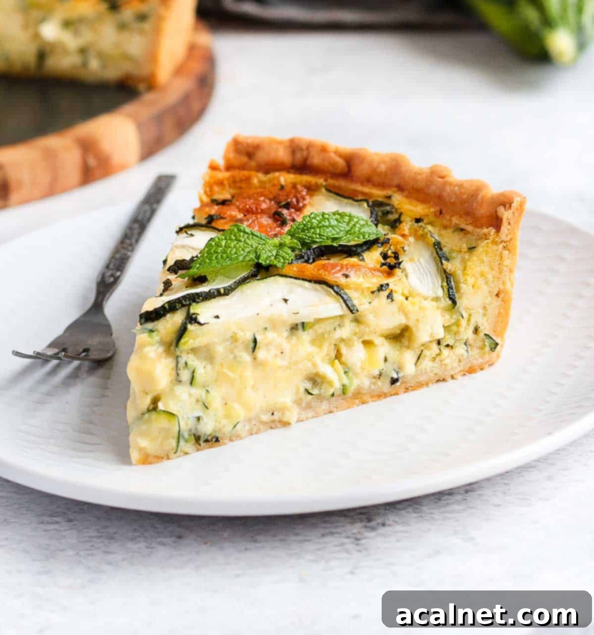 A single slice of Zucchini Quiche with Feta and Mint beautifully presented on a white plate, highlighting its layers and golden crust.