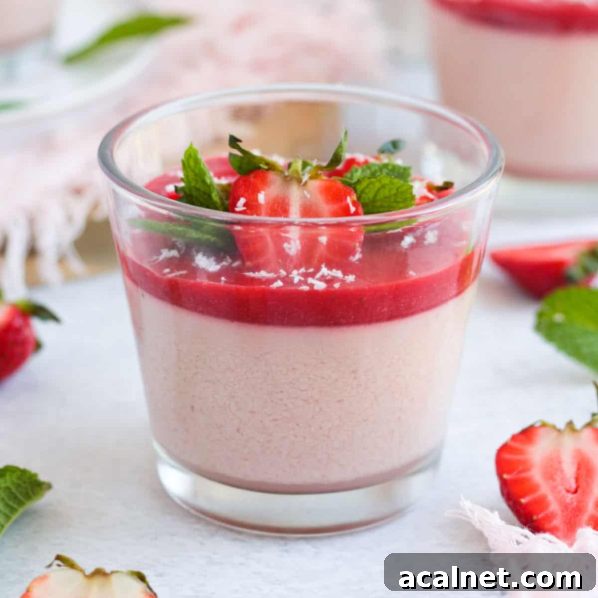 Close up on a elegant Strawberry Panna Cotta dessert in a glass, beautifully topped with fresh strawberries and a sprig of mint.