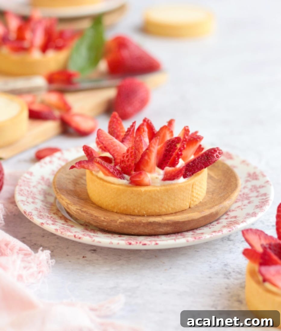 Close up on an individual strawberry tartlet surrounded by fresh strawberries, showcasing its beauty.