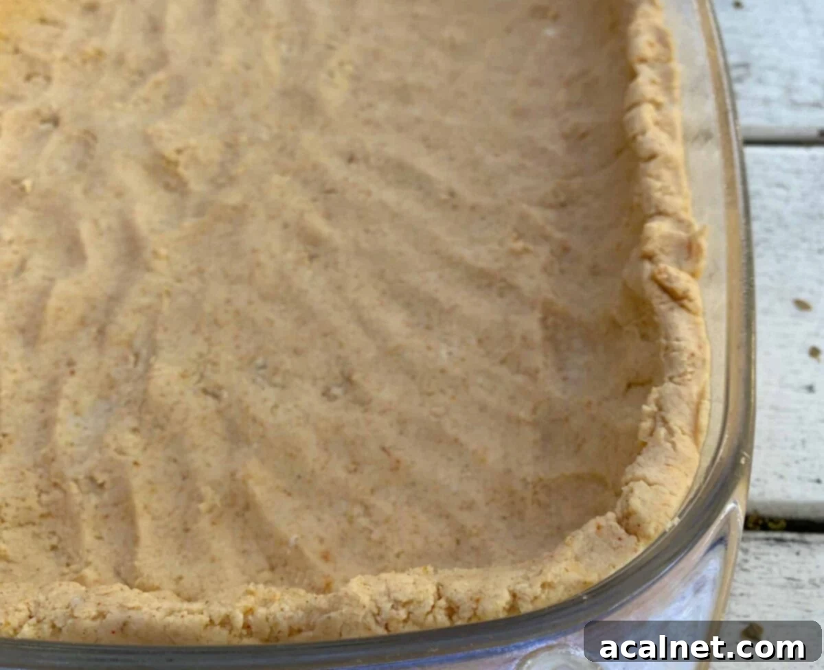 Tamale crust dough carefully patted up the sides of a clear glass casserole dish, forming a thick, even edge.