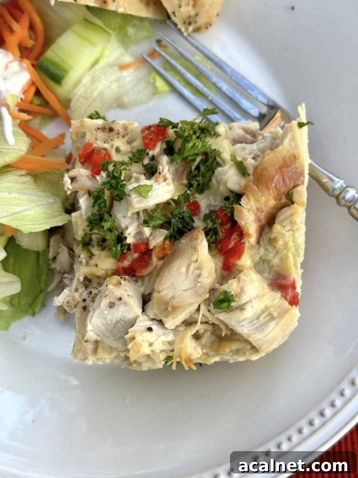 Chicken casserole on a plate with salad on the side and a fork on the plate.
