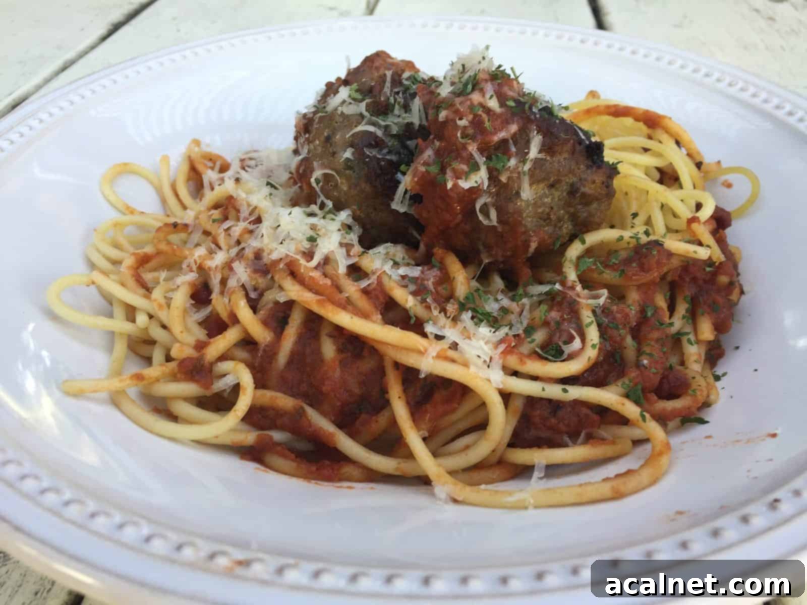 Meatballs on top spaghetti and sauce, with cheese garnish.