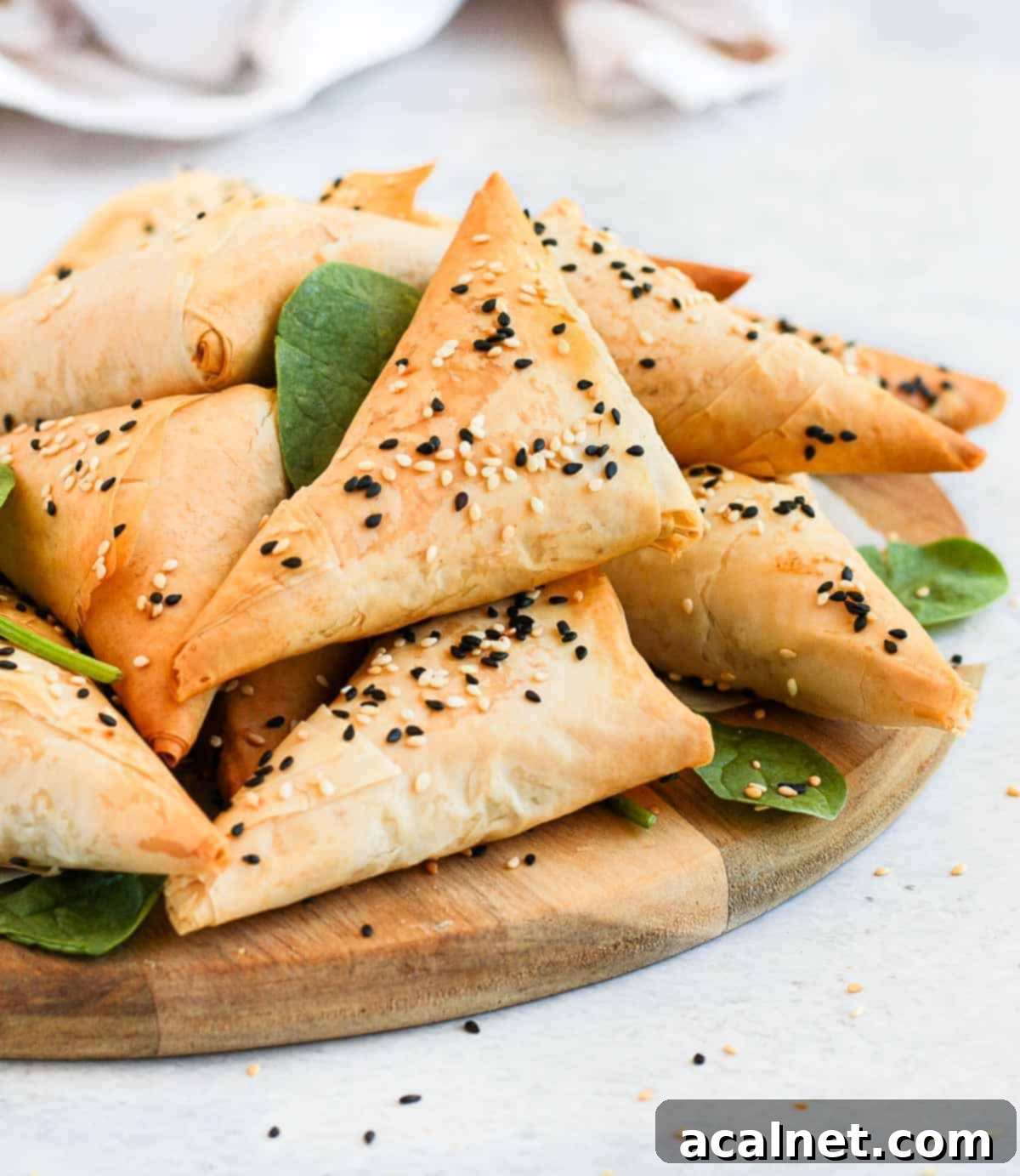 Crispy Golden Spanakopita Treats 4 Spinach and Feta triangles stacked on a wooden board,