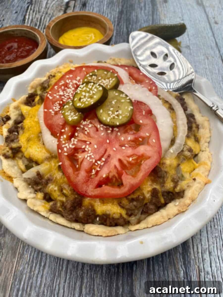 Cheeseburger pie in a pie plate with tomato and onion and sliced pickle on wooden planks, garnished with sesame seeds.