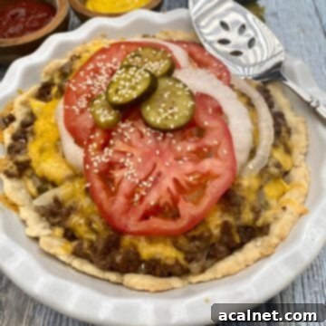 Delicious Cheeseburger pie in a pie plate, beautifully garnished with fresh tomato, onion, and sliced pickle on rustic wooden planks.