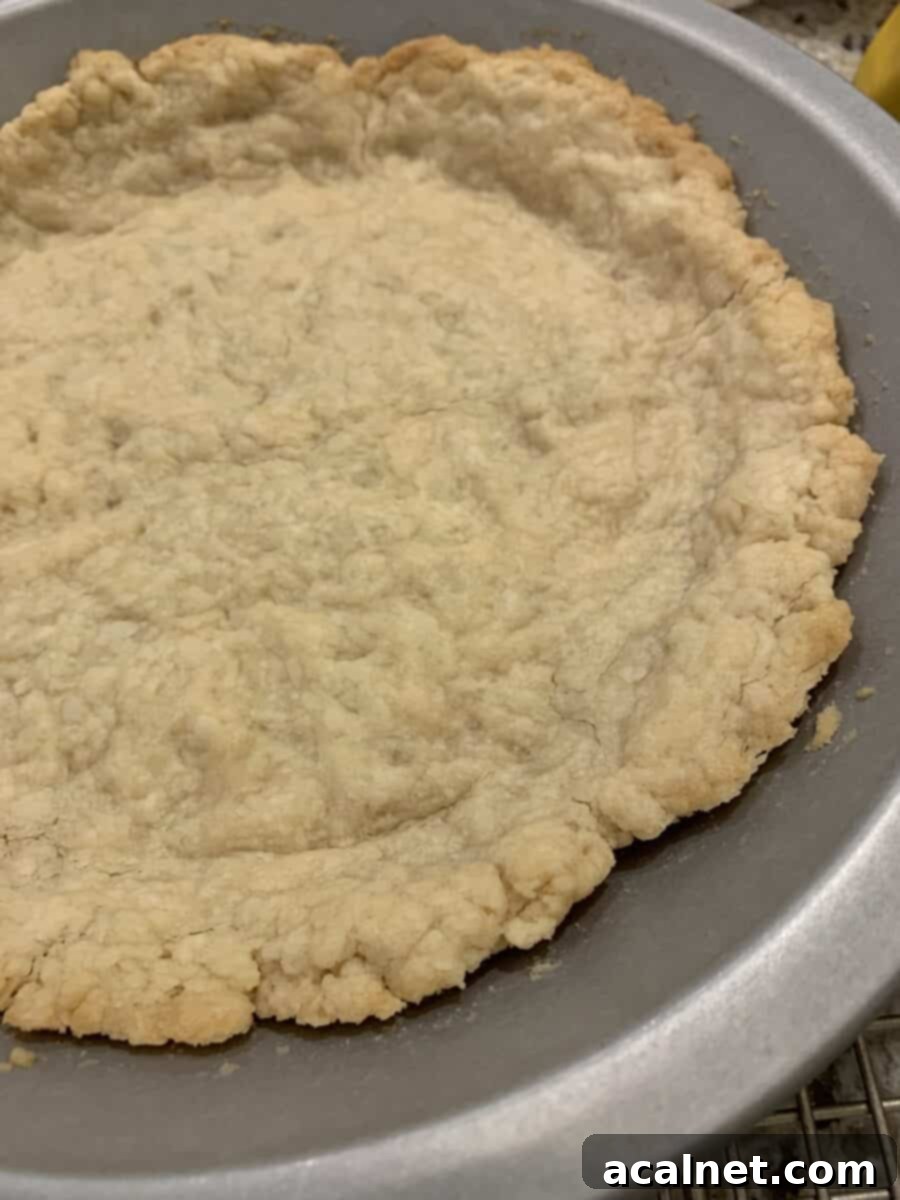 Golden brown, partially baked pie crust in a pie pan, freshly out of the oven, waiting for its filling.