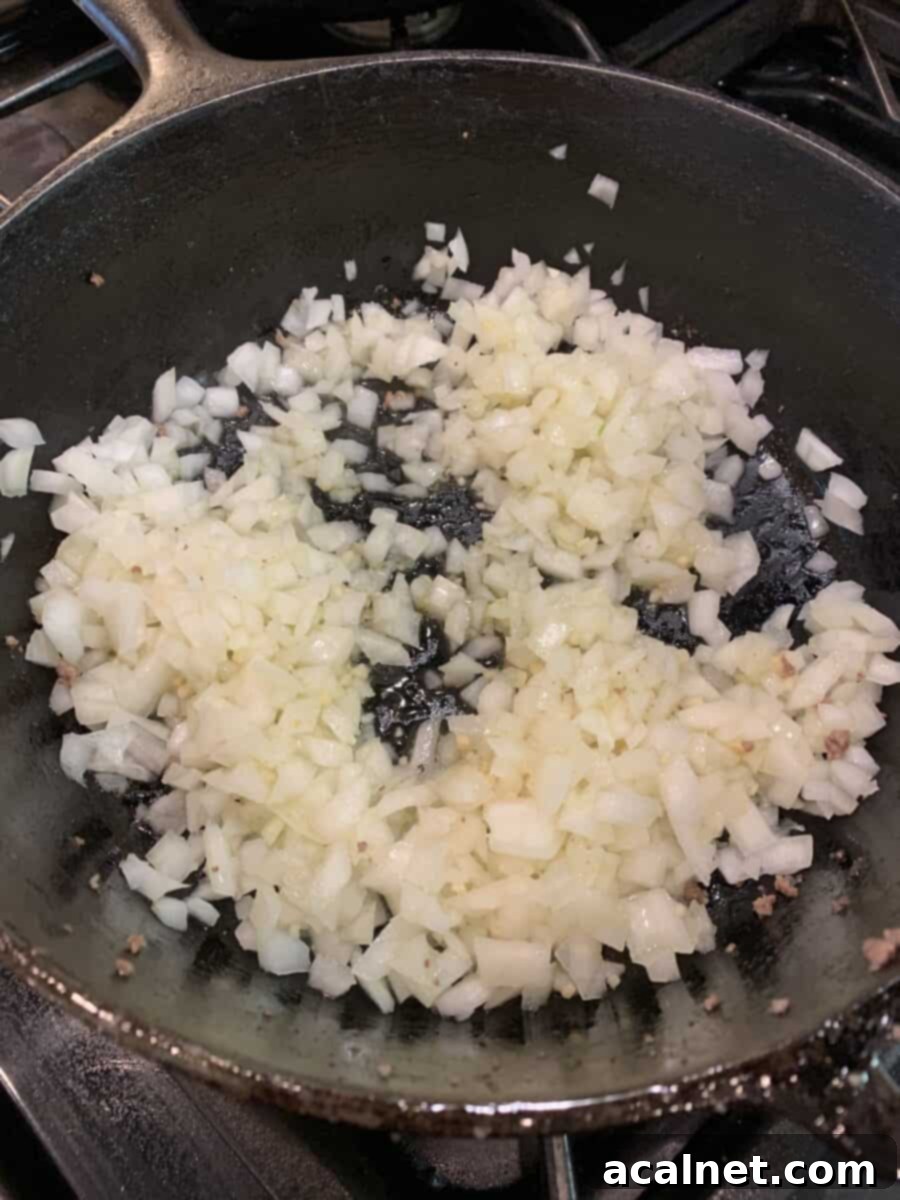 Finely diced onions cooking in a cast iron skillet, starting to caramelize and soften.