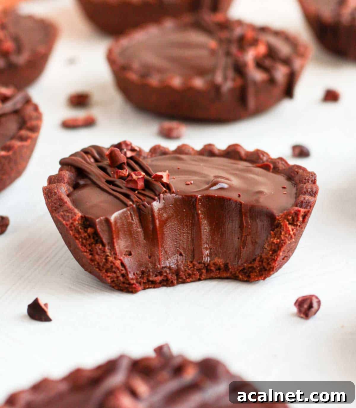 One chocolate tart on a white surface with a bite taken off.