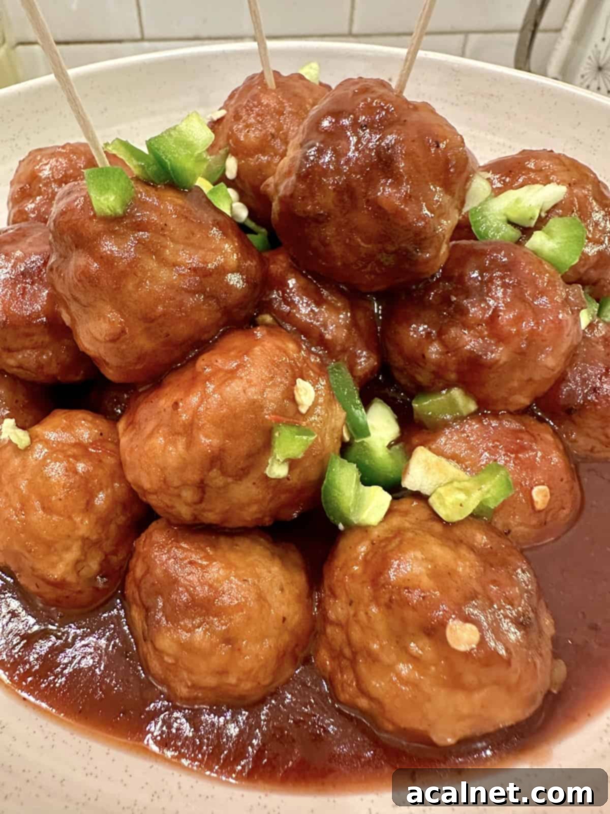 Sweet Heat Cranberry Jalapeño Meatballs 2 Meatballs in a serving bowl, garnished with fresh diced jalapeños.