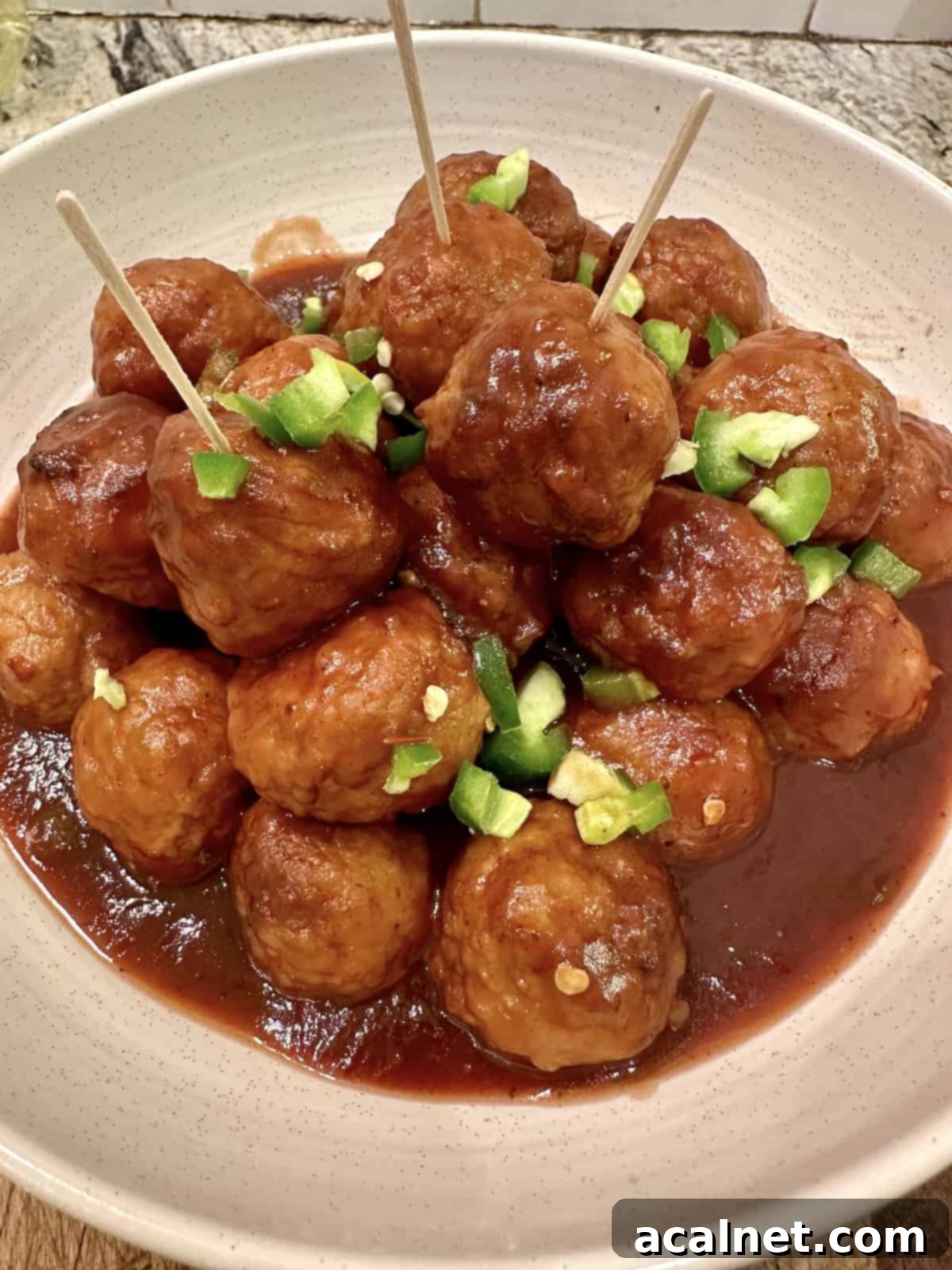 Sweet Heat Cranberry Jalapeño Meatballs 8 Cranberry meatballs in a serving bowl with diced peppers and fresh herbs.
