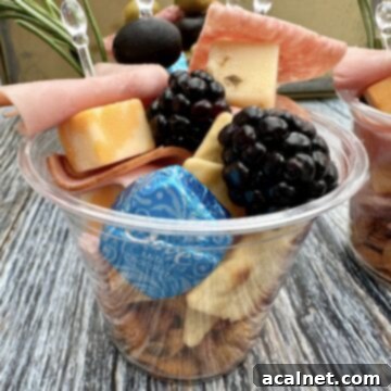 Cheese, crackers, meat, olives stacked in a cup.