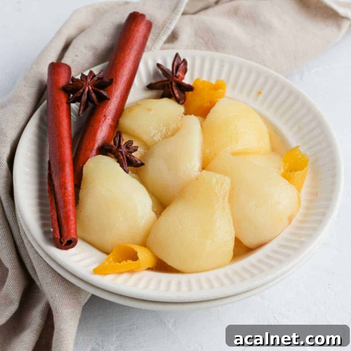 Stewed Pears in a white bowl with cinnamon, star anise and orange peels.