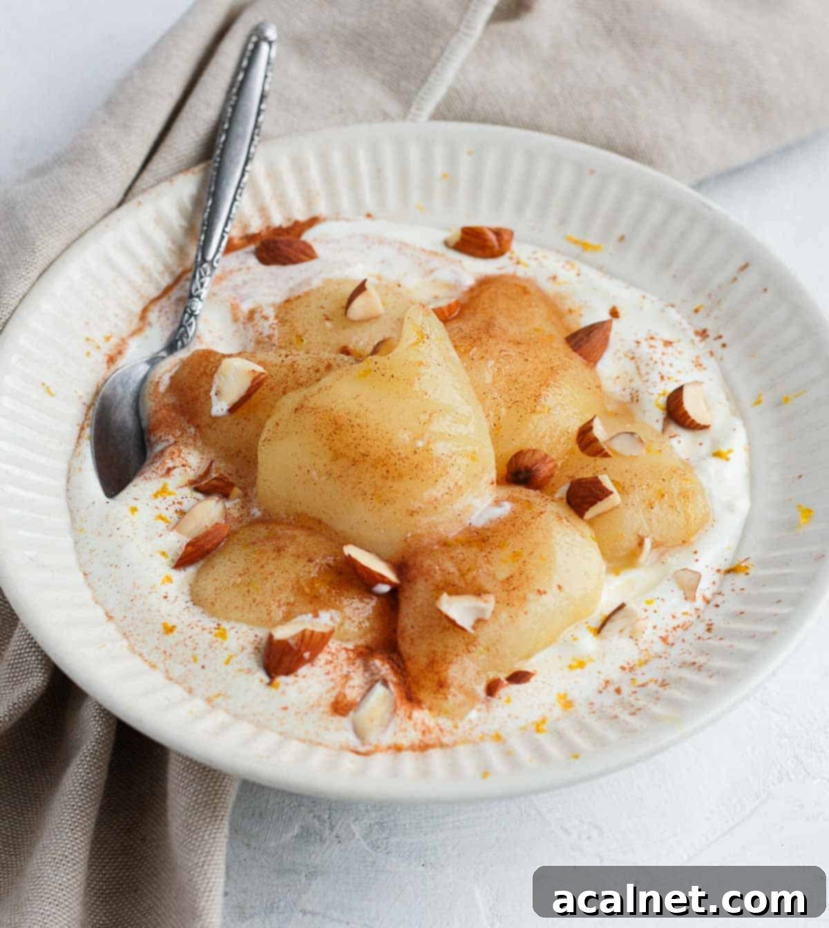 Poached pears over yogurt in a white bowl.