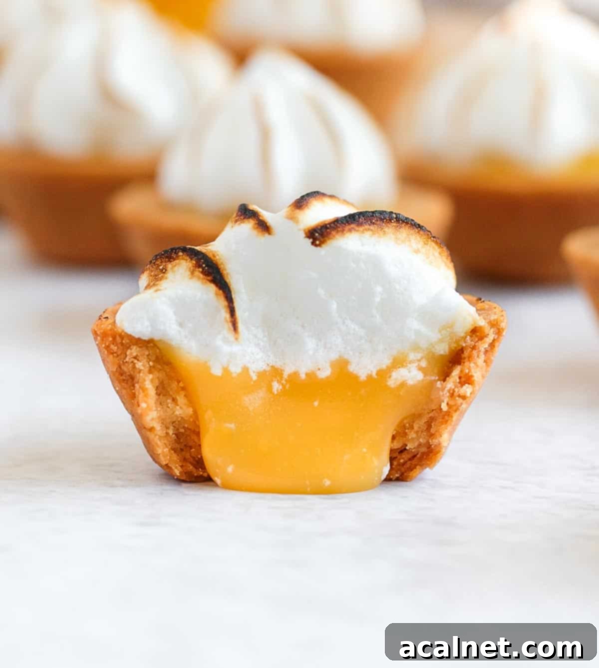 One bite taken off a mini tart with lemon curd pouring out.