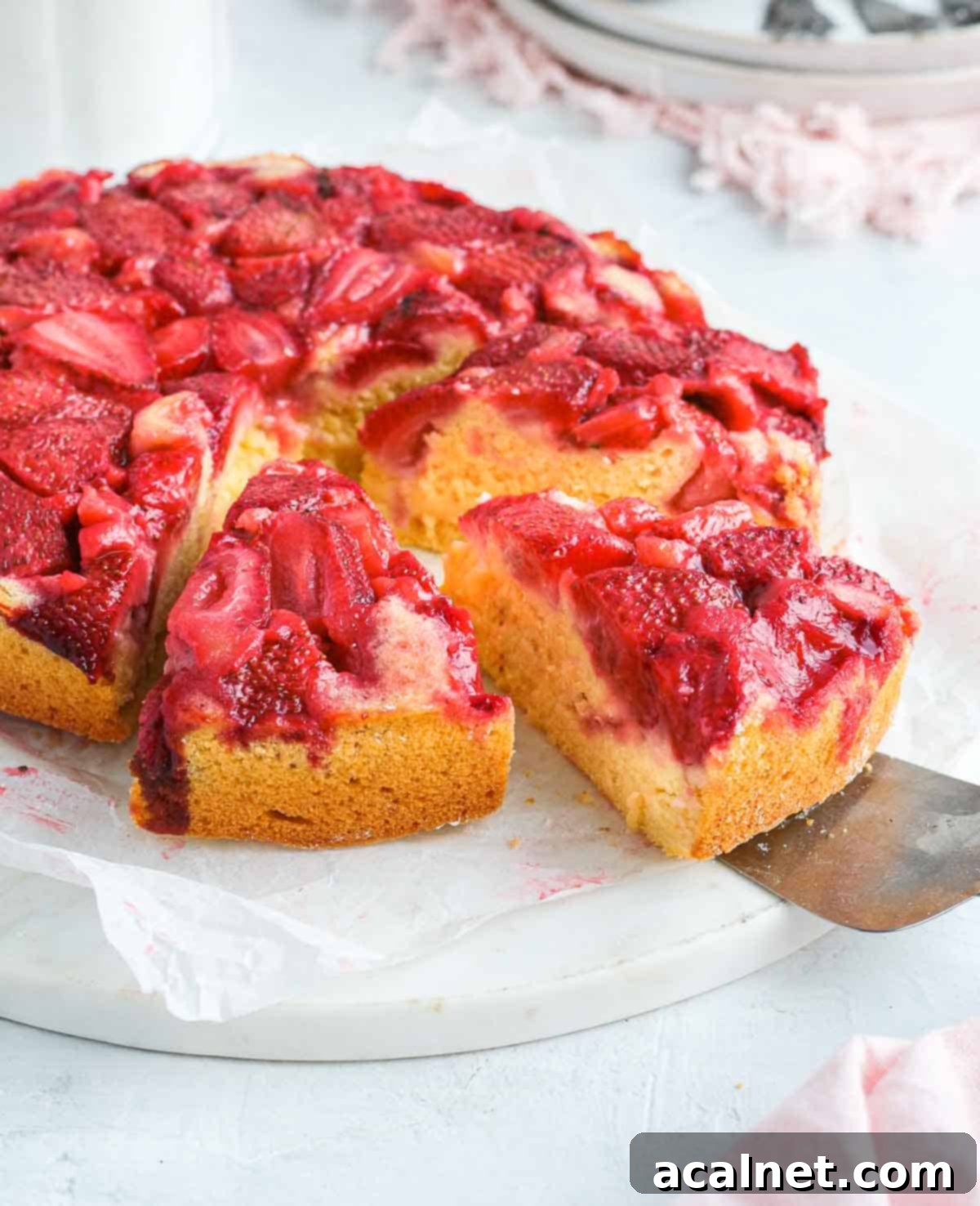 A serving spoon taking one slice of Strawberry Upside Down Cake from a pan.