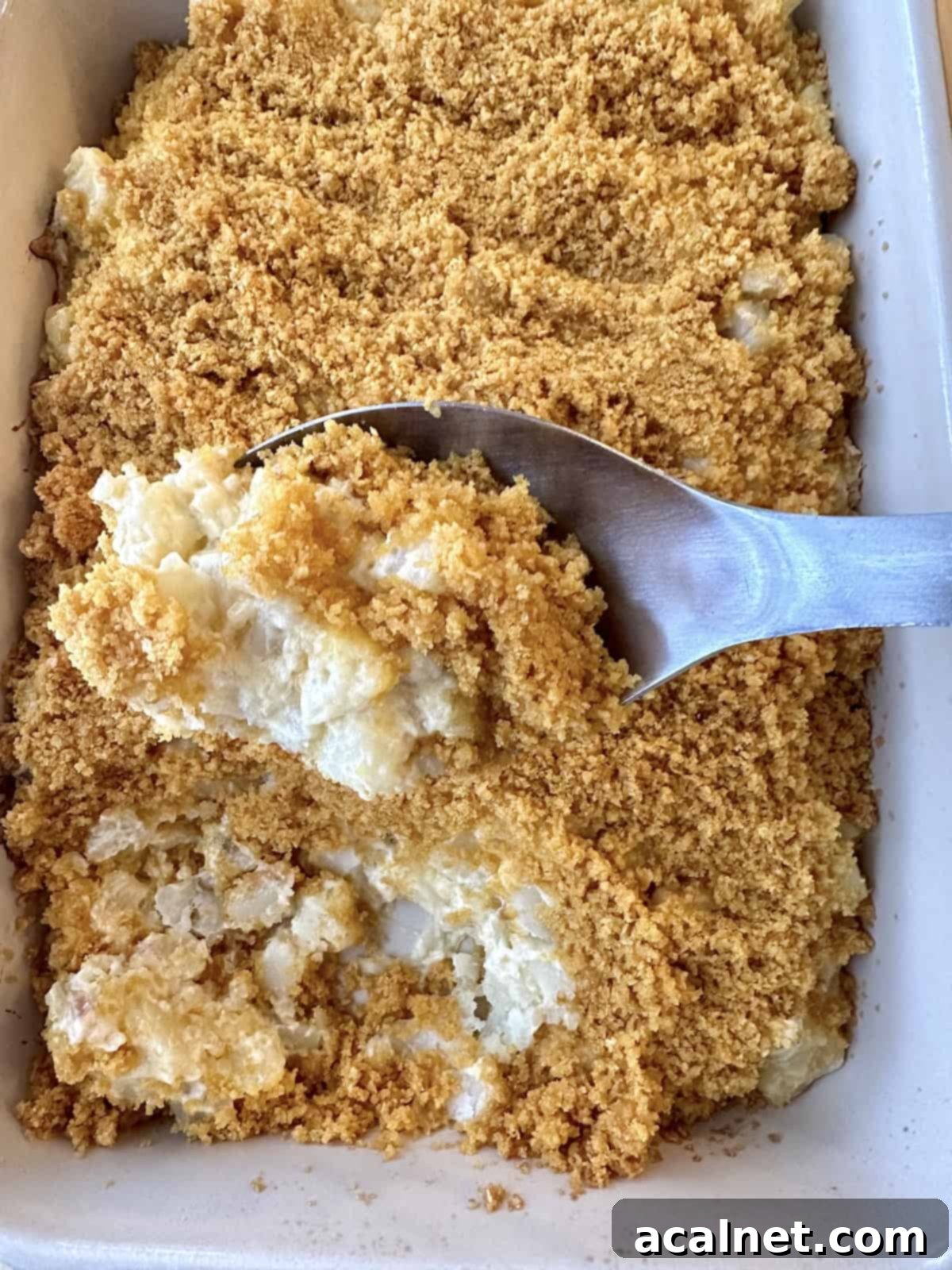 Golden Crunch Cheesy Potatoes 2 A serving spoon scooping up a serving of potato casserole from a baking dish, showcasing the creamy potatoes and crispy topping.