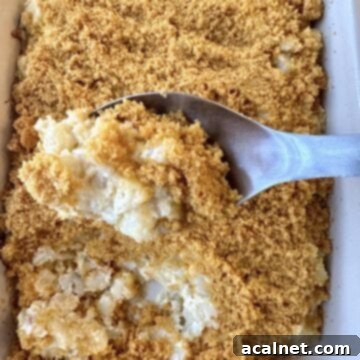 Golden Crunch Cheesy Potatoes 9 A serving spoon scooping up a serving of potato casserole from a baking dish, with the crispy corn flake topping visible.