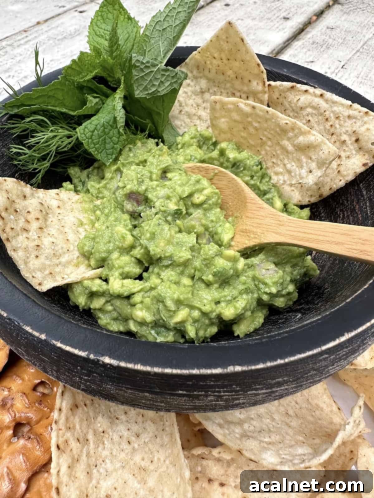 Fresh guacamole in a bowl with chips, fresh herbs and a small spoon dishing up a portion.