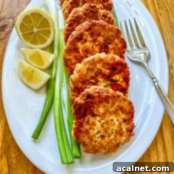 Cooked salmon patties on a plate with scallions, lemons and a fork.