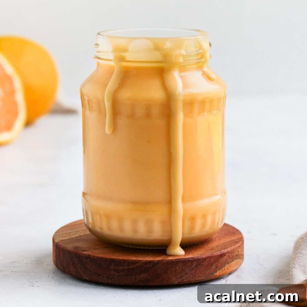 Lustrous homemade orange curd in a clear glass jar, with enticing drips running down the side, signifying its creamy texture.