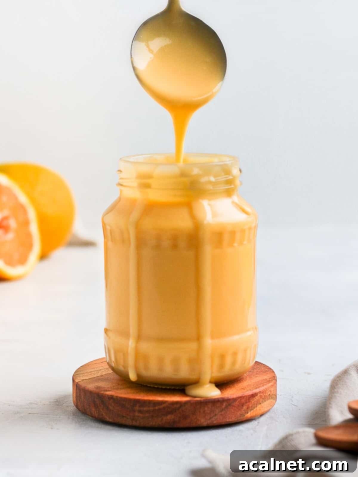 Smooth and vibrant orange curd gracefully dripping from a spoon into a clear glass jar, illustrating its perfect, flowing consistency.