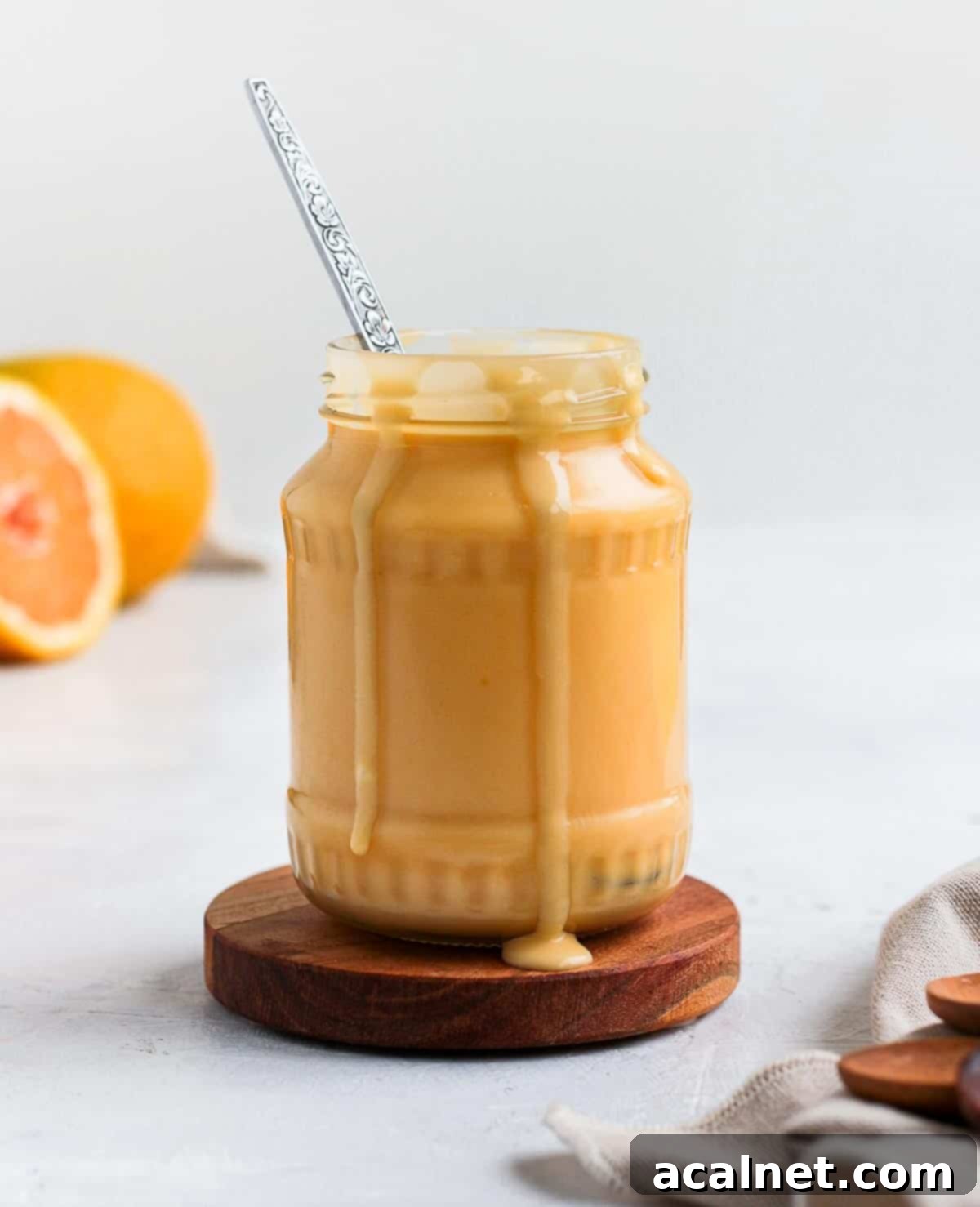 A glass jar filled with luscious orange curd, with a spoon nestled inside, inviting you to taste its smooth texture.