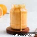 Lustrous homemade orange curd in a clear glass jar, with enticing drips running down the side, signifying its creamy texture.