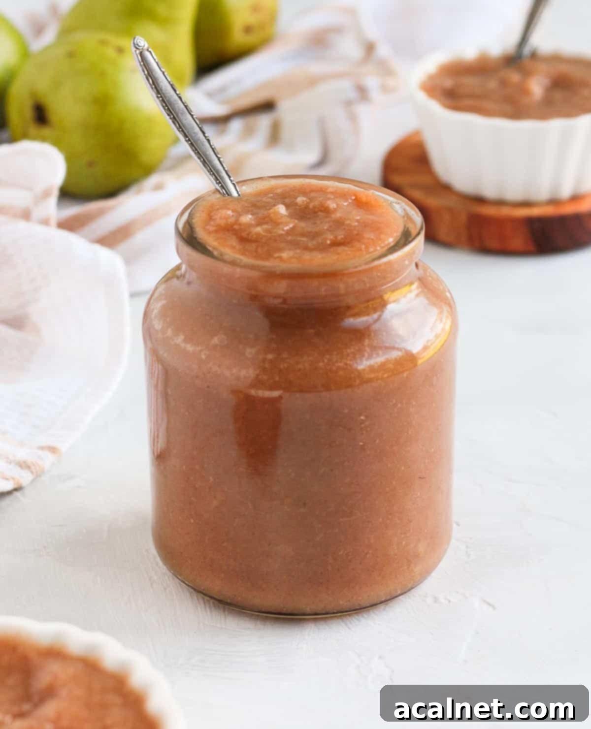 Smooth spiced pear compote served in an elegant glass jar with a silver spoon, invitingly ready to be enjoyed.