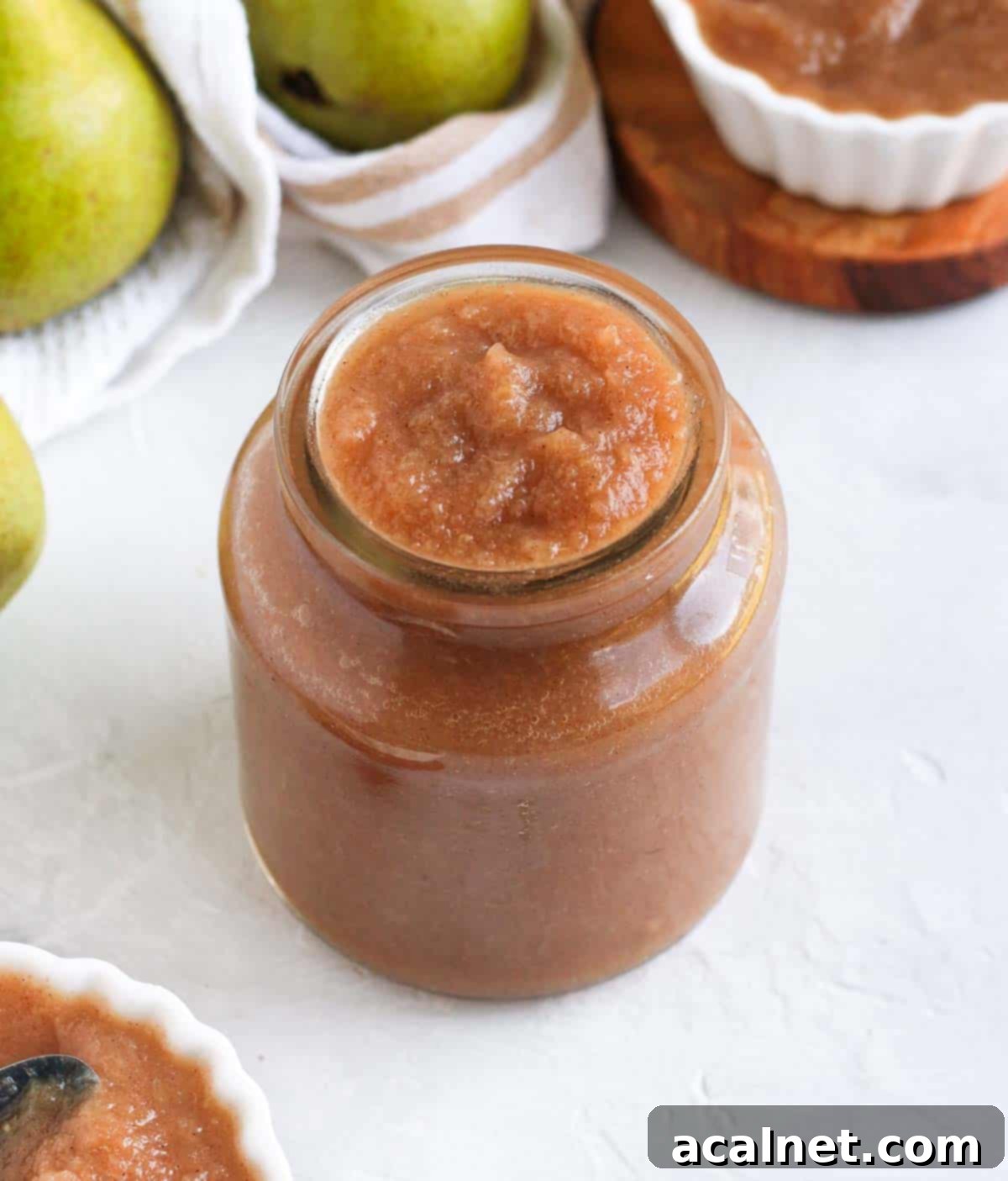 Freshly made pear compote in a clear glass jar, resting on a pristine white surface, beautifully showcasing its radiant golden hue and enticing smooth texture.