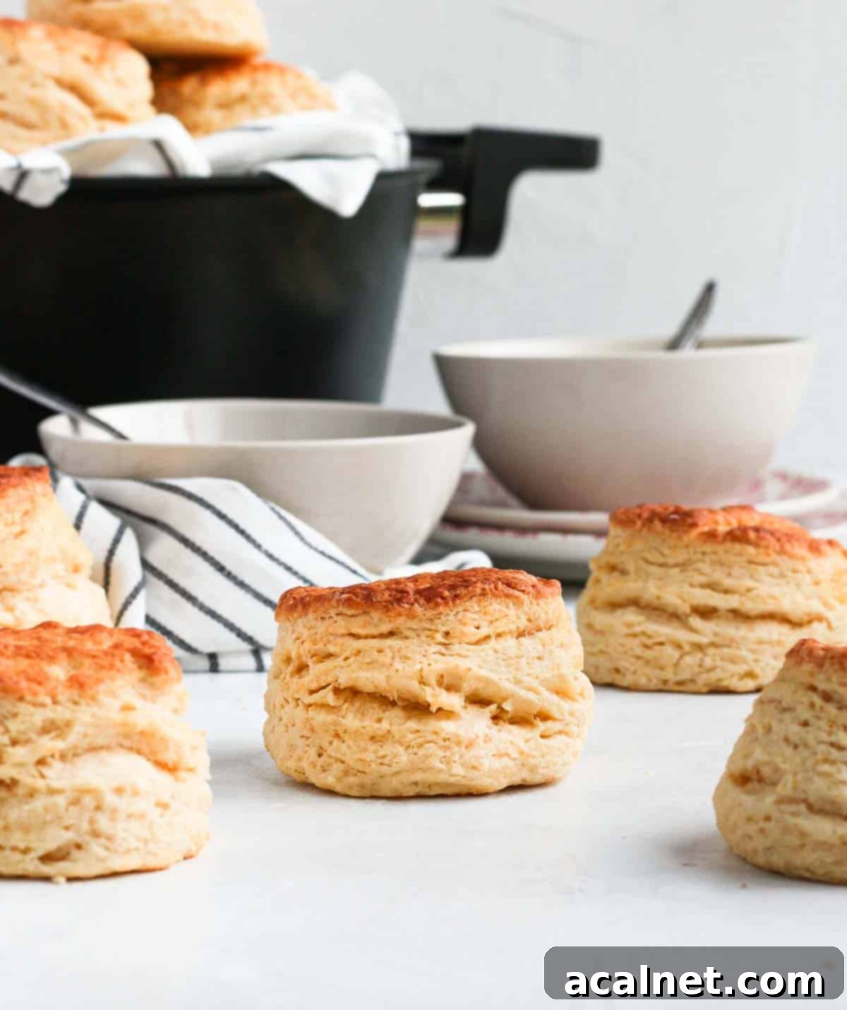 Easy Remoska Scones 4 Scones on a white surface with two white bowls and the remoska in the background.