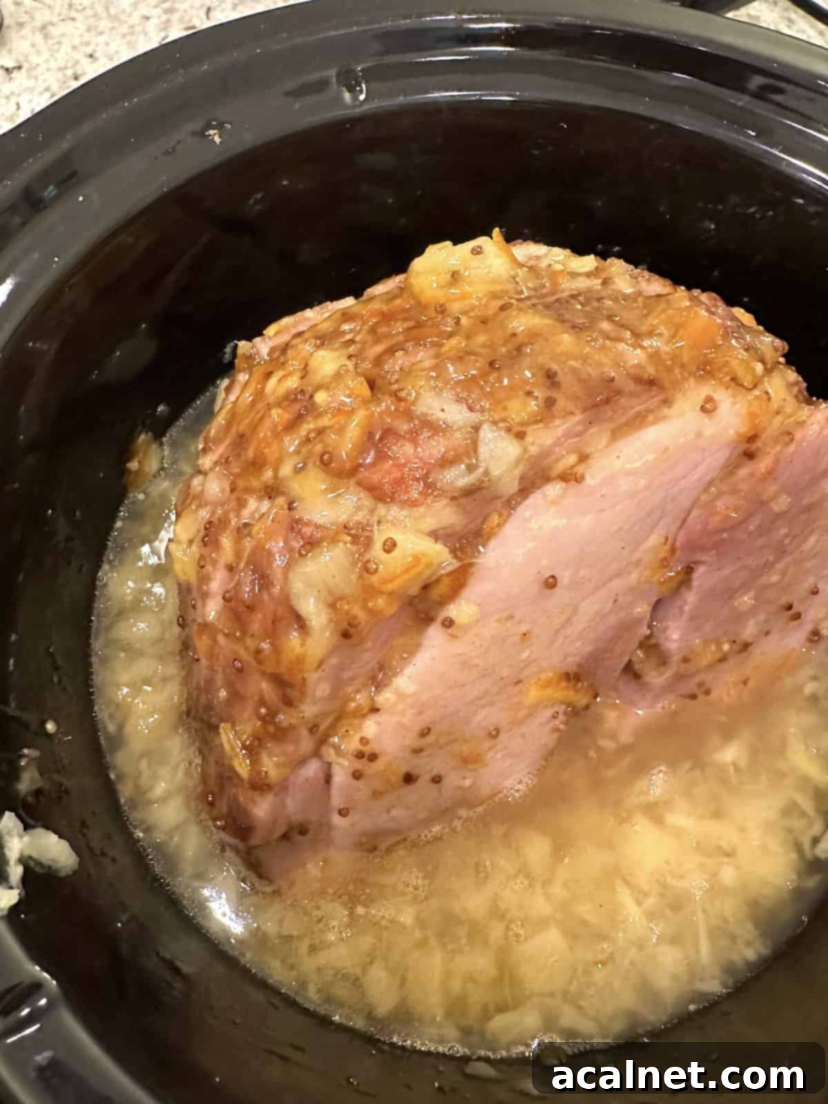 A beautifully cooked ham with a golden marmalade and pineapple glaze, garnished with crushed pineapple around its base.