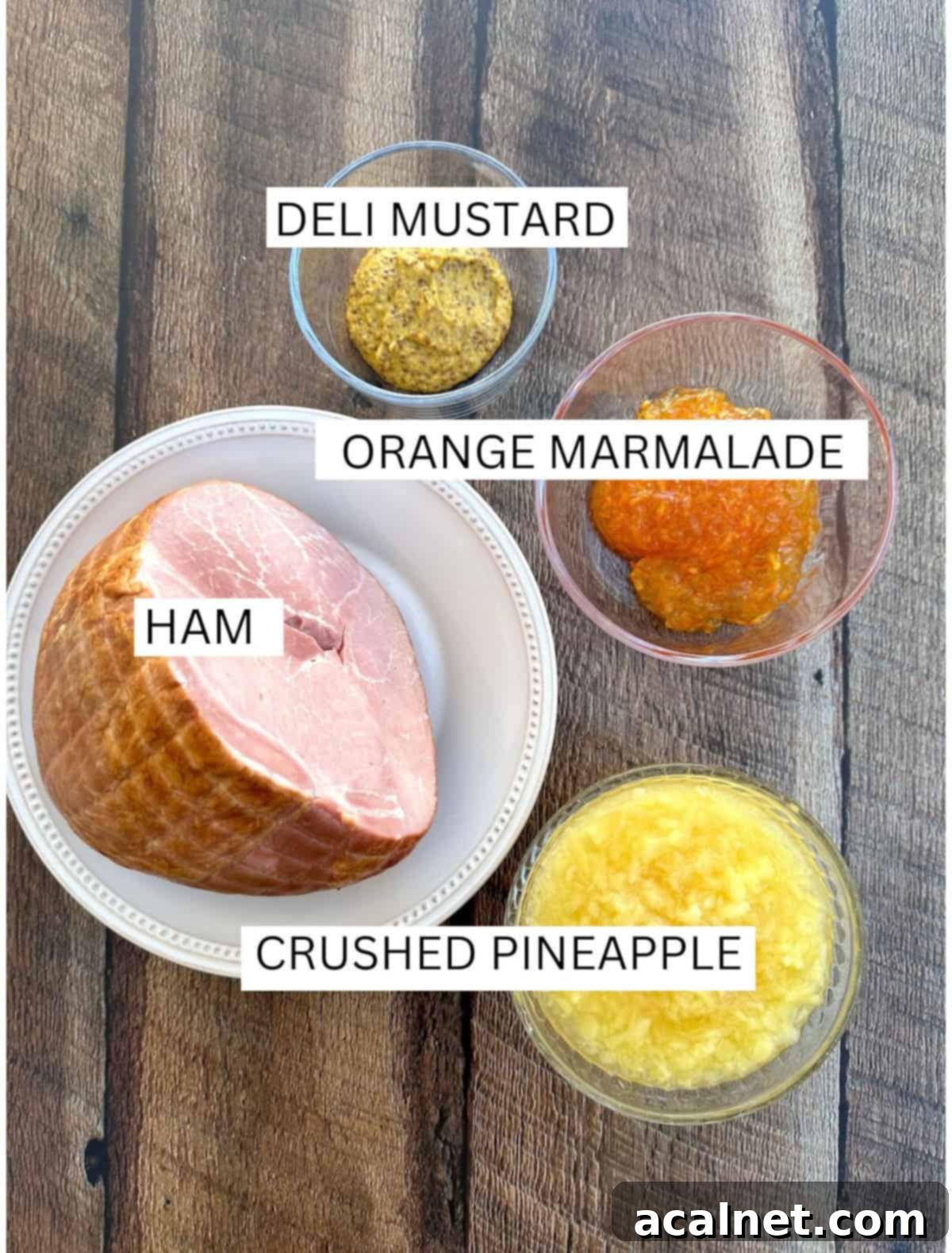 Ingredients for marmalade glazed ham laid out on a table, including a ham, a can of crushed pineapple, orange marmalade, and deli mustard.