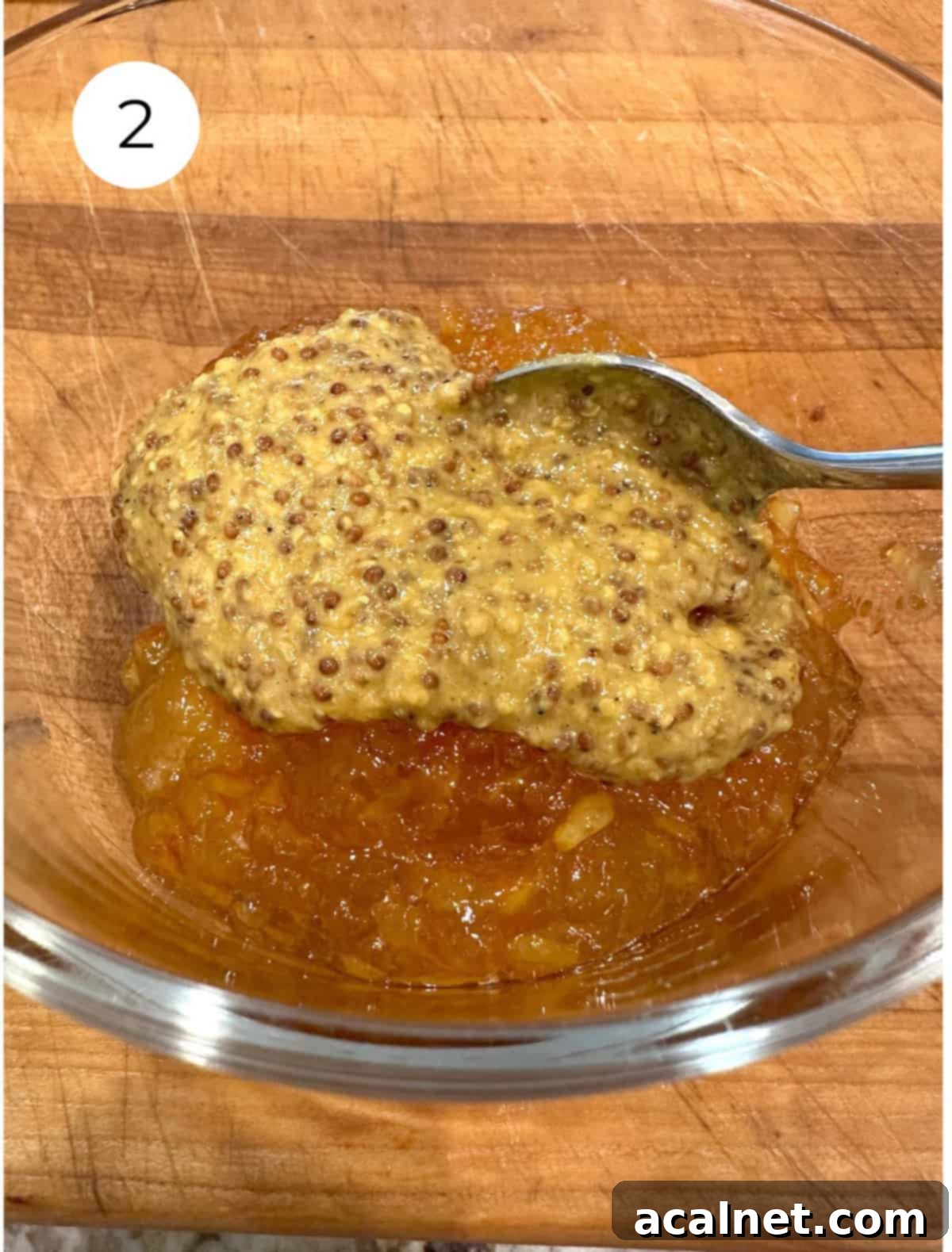 Orange marmalade and deli mustard being mixed together in a small bowl with a spoon, forming the ham glaze.