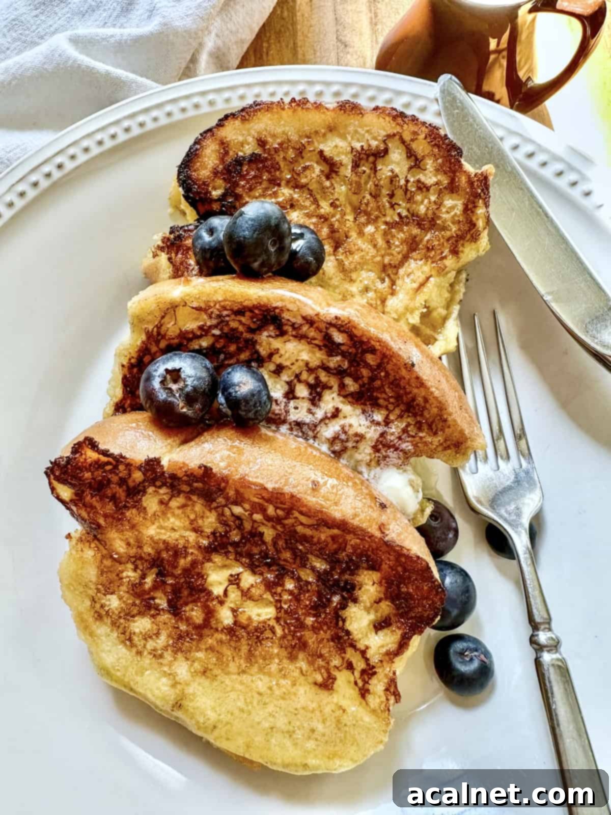 Three slices of buttermilk french toast on a plate with fresh berries on top, garnished with a dusting of powdered sugar.