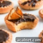 One chocolate orange tartlet with a bite taken off, showing the layers of ganache, curd, and pastry, ready to be enjoyed.