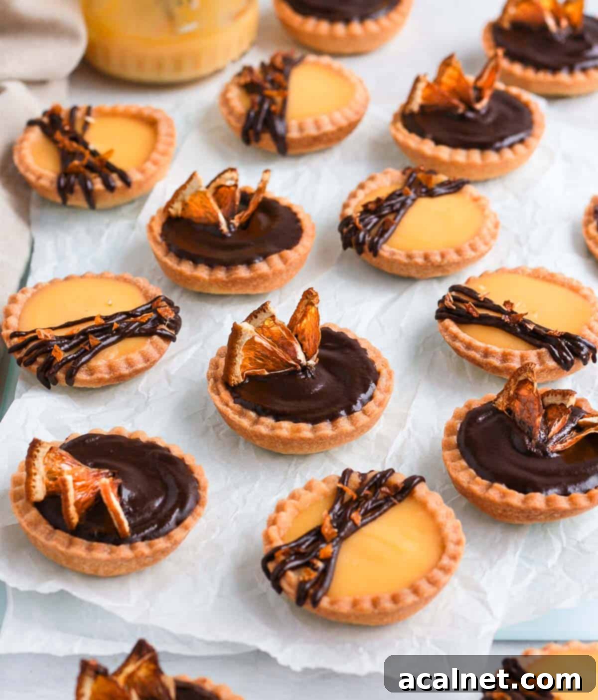 Several finished Chocolate Orange Tartlets arranged beautifully on a white sheet of baking paper, ready for serving.
