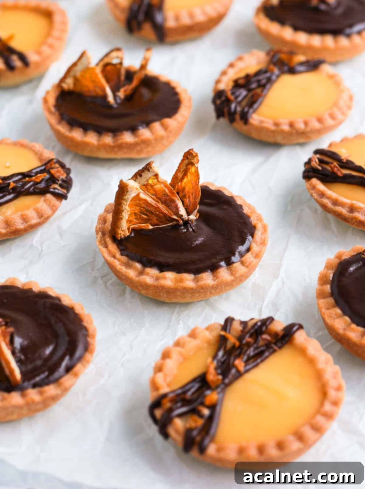 Several Chocolate Orange Tartlets arranged neatly on white baking paper, ready to be picked up and enjoyed.