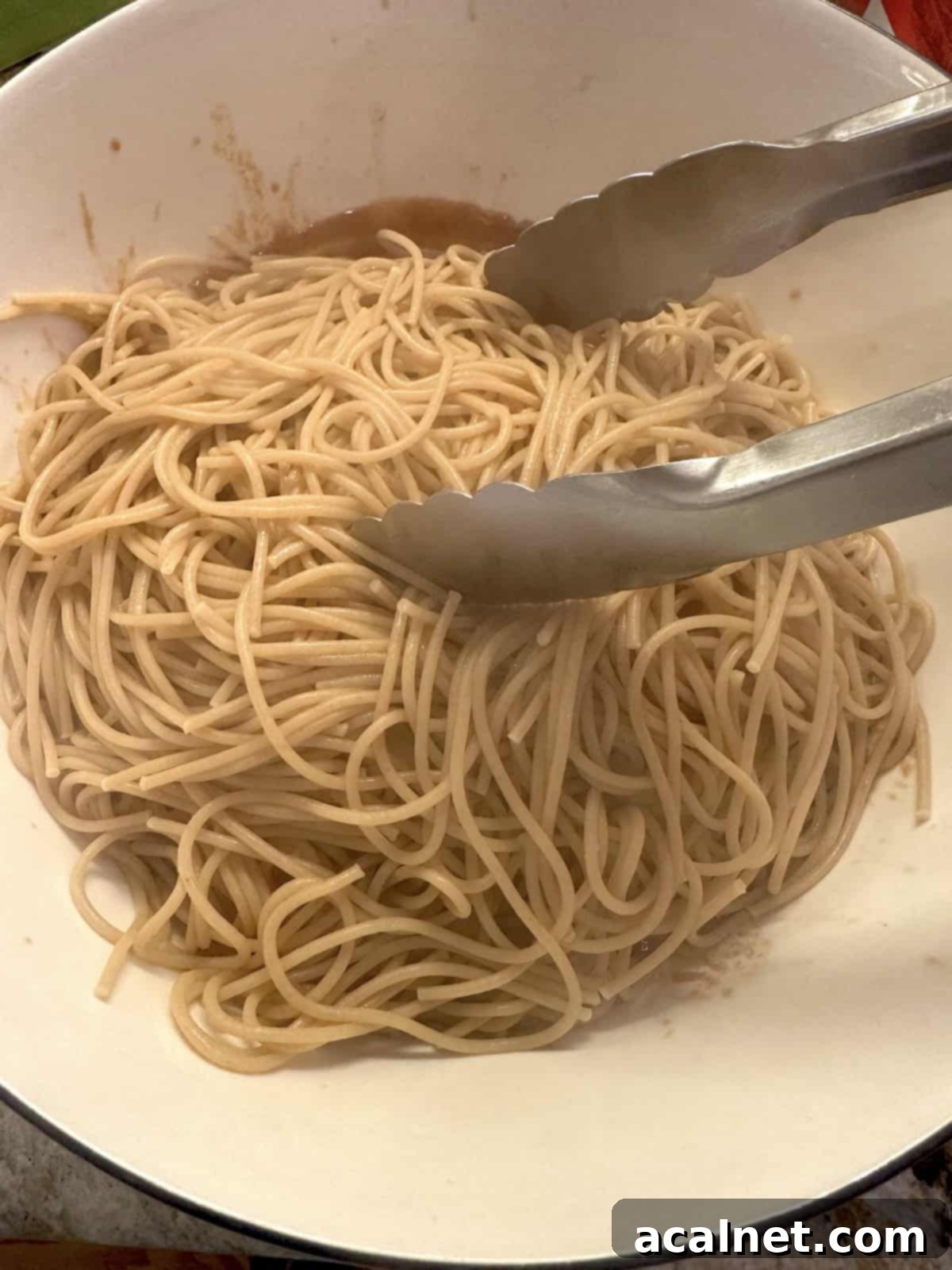 Cooked spaghetti in a bowl with tongs.