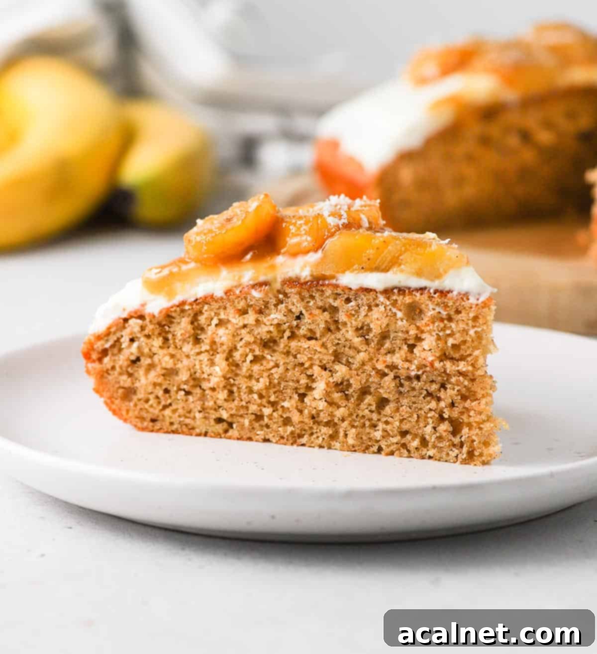 One perfect slice of Remoska Banana Bread Cake with Cream Cheese Frosting and Caramelized Bananas, served on a white plate.