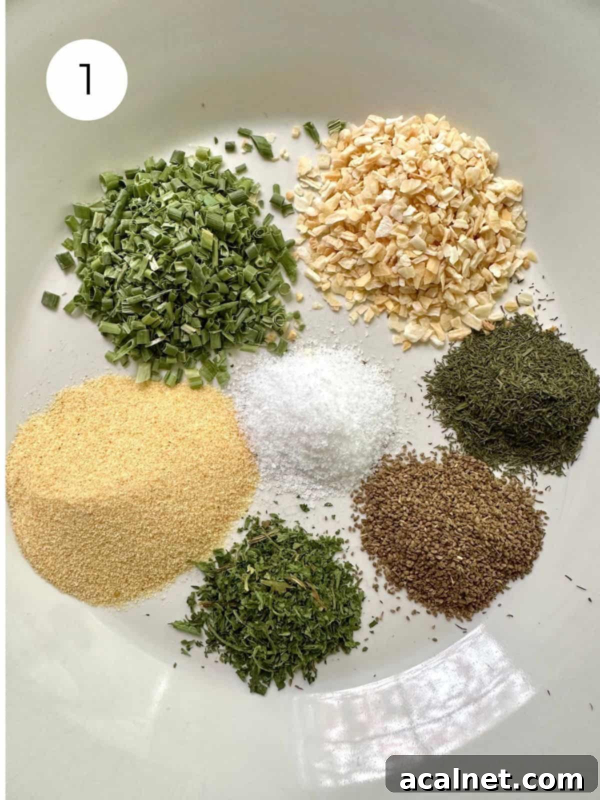 Small mounds of various dried herbs and salt neatly portioned on a white plate, ready for mixing.