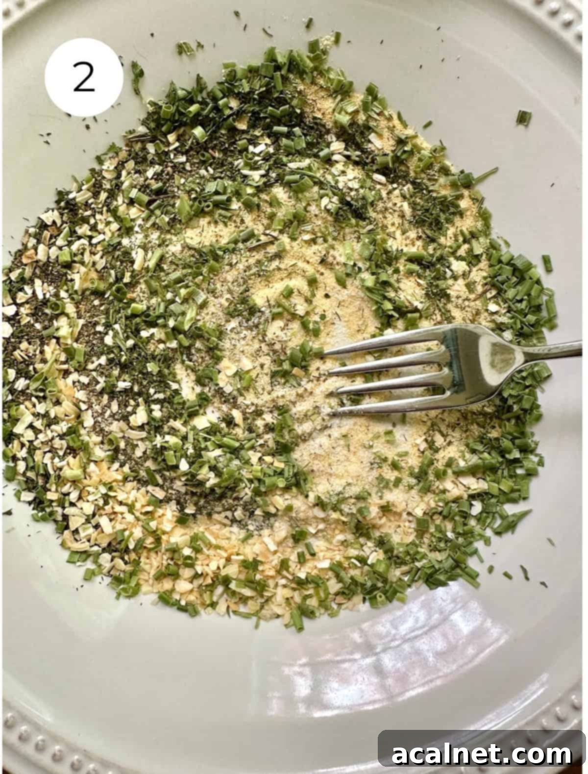 A fork gently blending a mixture of dried herbs and salt on a pristine white plate, creating a uniform spice blend.