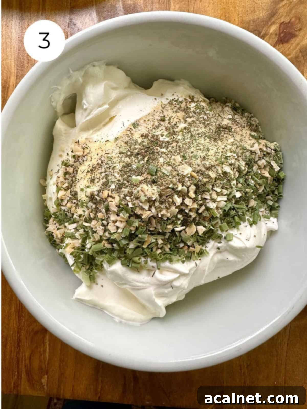 A generous dollop of creamy sour cream in a bowl, topped with a vibrant sprinkle of blended dried herbs, waiting to be mixed.