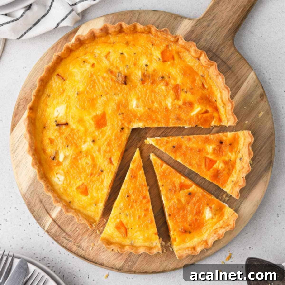 Flatlay of the pumpkin quiche on a wooden board with 3 slices cut off.