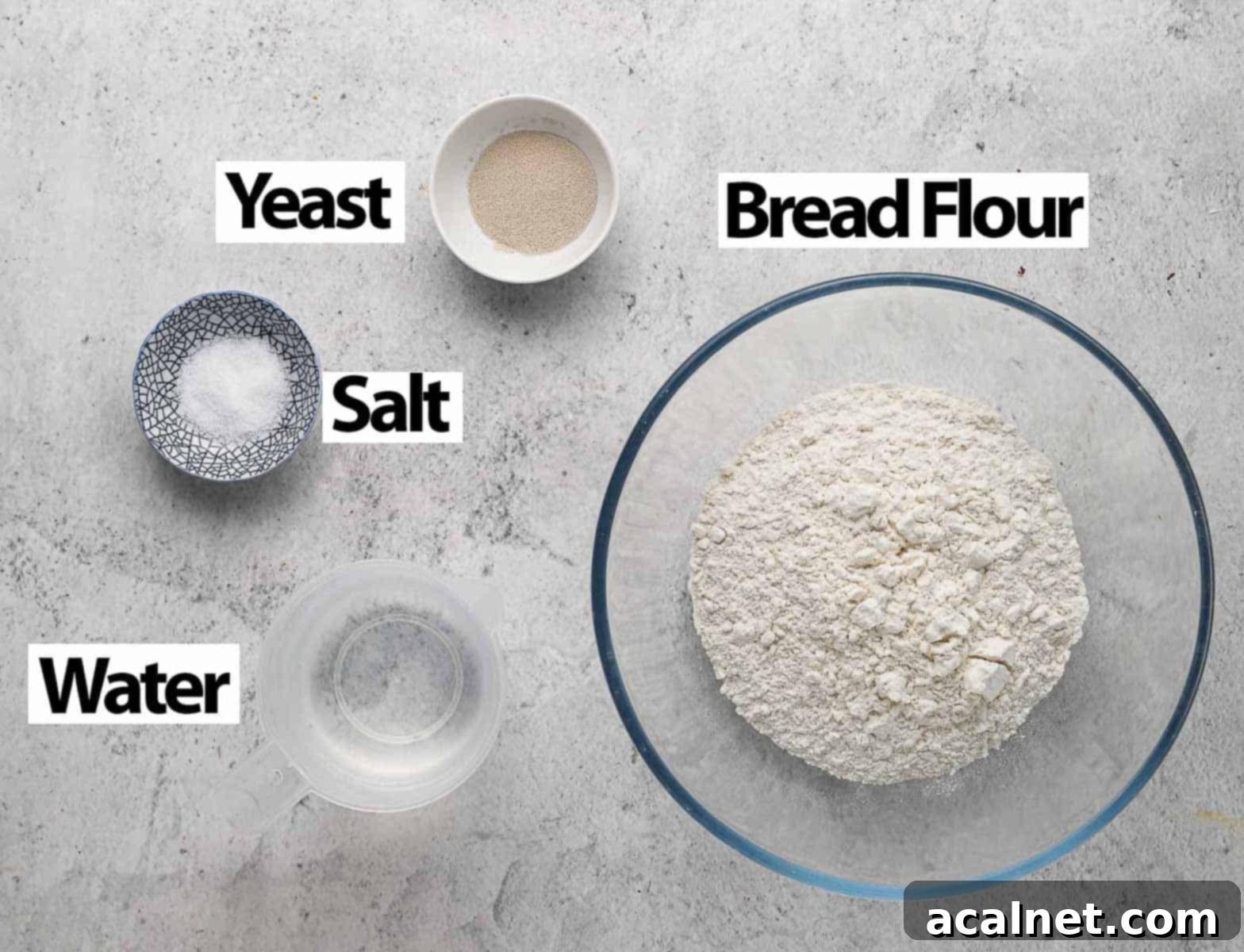 No Knead Bread in the Remoska 3 Ingredients for no-knead bread: flour, salt, yeast, and water, laid out on a grey surface.