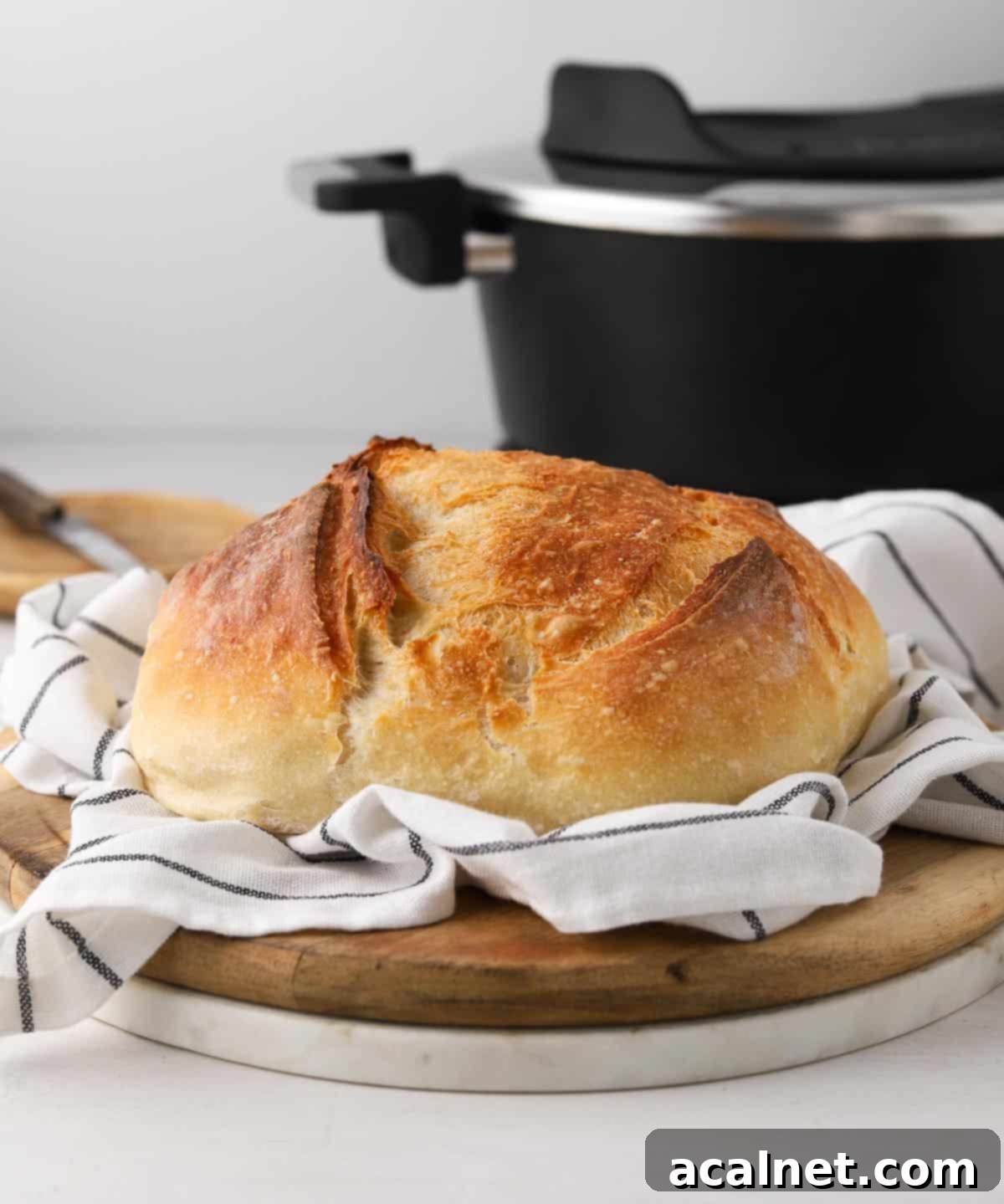 No Knead Bread in the Remoska 8 Freshly baked No-Knead bread cooling on a hand towel with the Remoska Tria in the background.