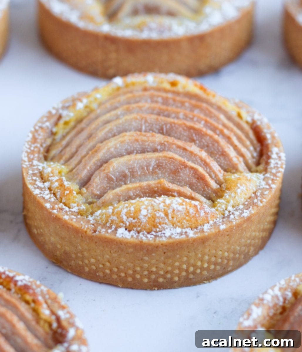 One pear tartlet on a grey surface surrounded by more tarts, indicating the need for specific baking pans.