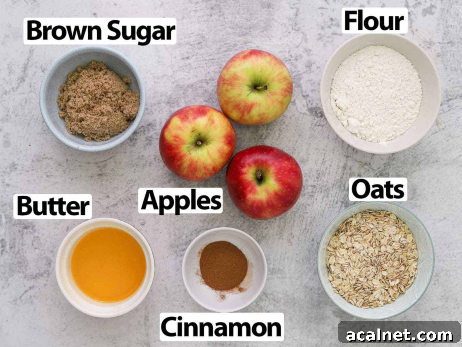 Remoska's Golden Crumble-Baked Apples 3 A selection of fresh baking ingredients including flour, oats, brown sugar, cinnamon, butter, and ripe apples, arranged on a grey surface.